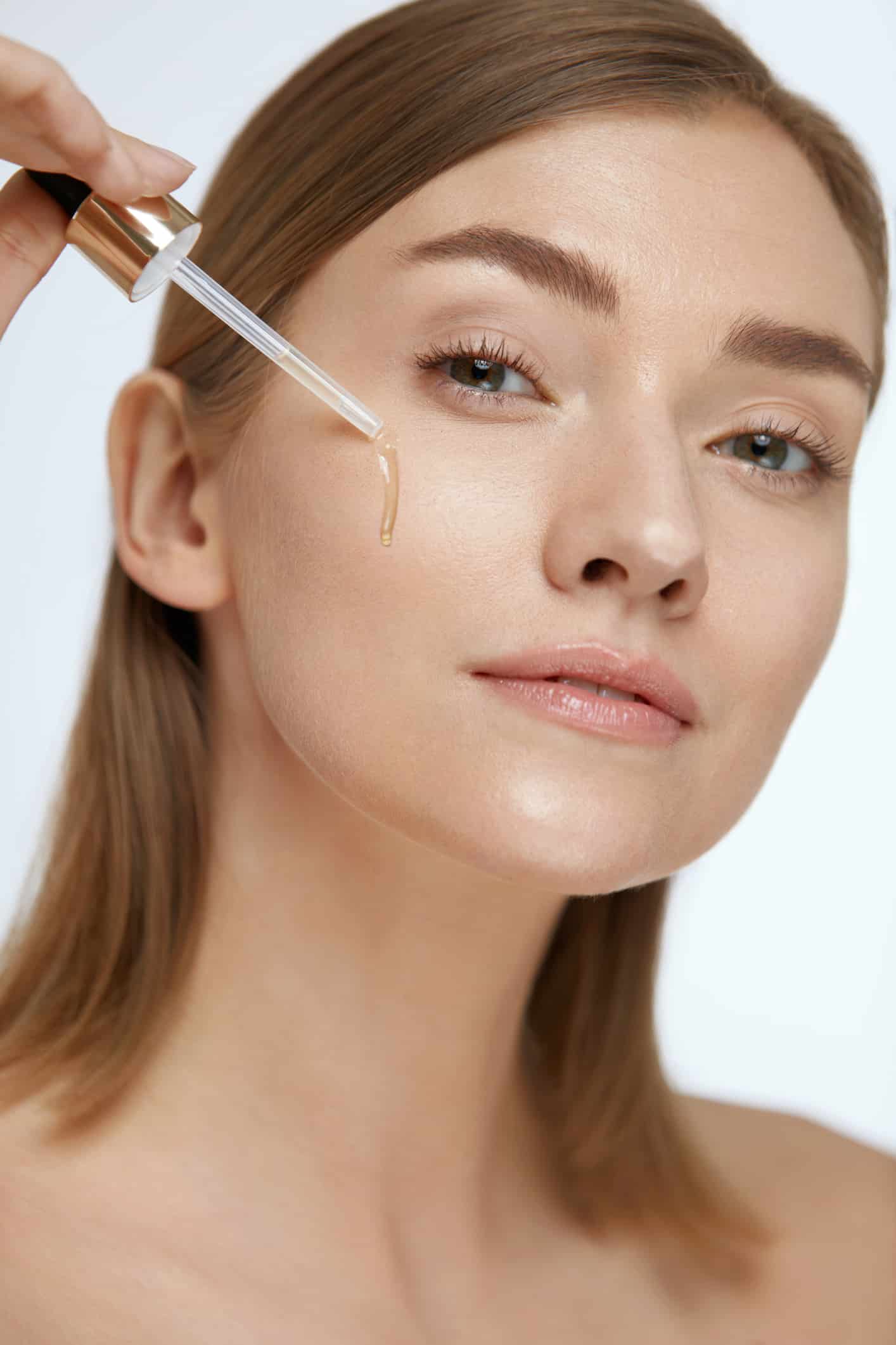 Skin care. Woman applying serum or facial oil on beauty face closeup. Girl model applying essence on white background