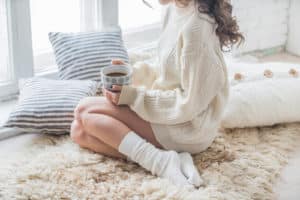 woman in knit sweater sitting at home with hot chocolate